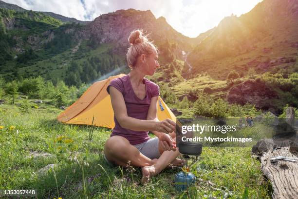 female hiker at campsite preparing lunch by the lake - camping stove stockfoto's en -beelden