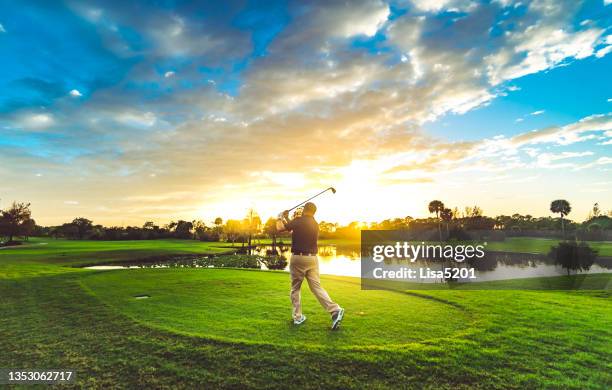 man on a idyllic scenic golf course swinging golf club at sunset - golf swing sunset stock pictures, royalty-free photos & images