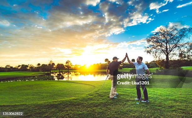 deux golfeurs masculins high five sur un parcours de golf pittoresque au coucher du soleil - parcours photos et images de collection