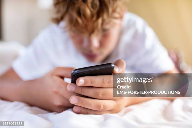 teenager boy is using smartphone at home in bed - jongens stockfoto's en -beelden