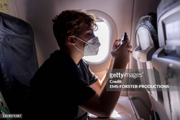 teenager boy is using smartphone in airplane - protective face mask foto e immagini stock