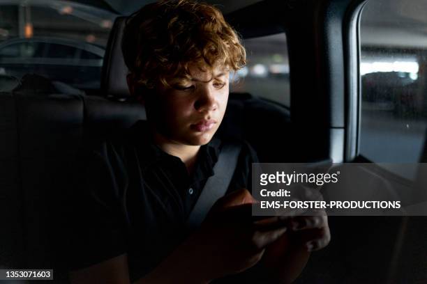teenager boy is using smartphone in car - seat perilous stock-fotos und bilder
