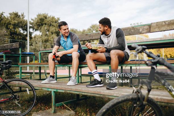 two young male cyclists taking a break of bicycle ride in the city park - adult riding bike through park stock pictures, royalty-free photos & images