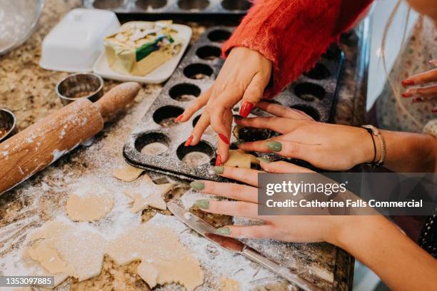 close-up of two young woman in a kitchen, baking mince pies in a christmassy scene - christmas preparation stock pictures, royalty-free photos & images