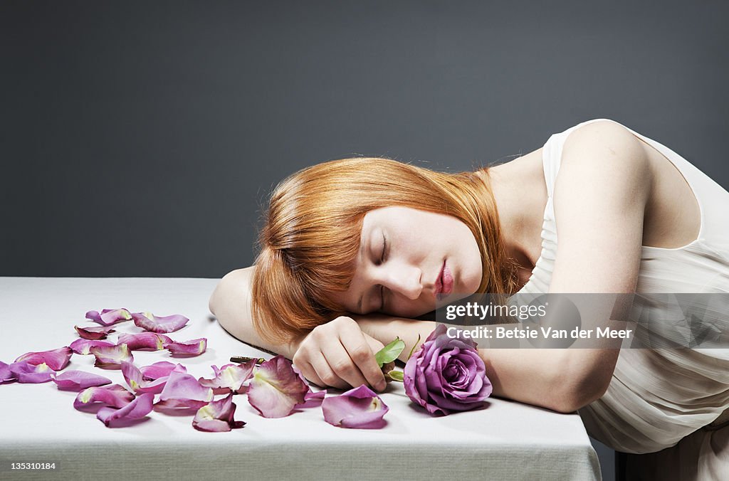 Woman resting head on table, holding rose.