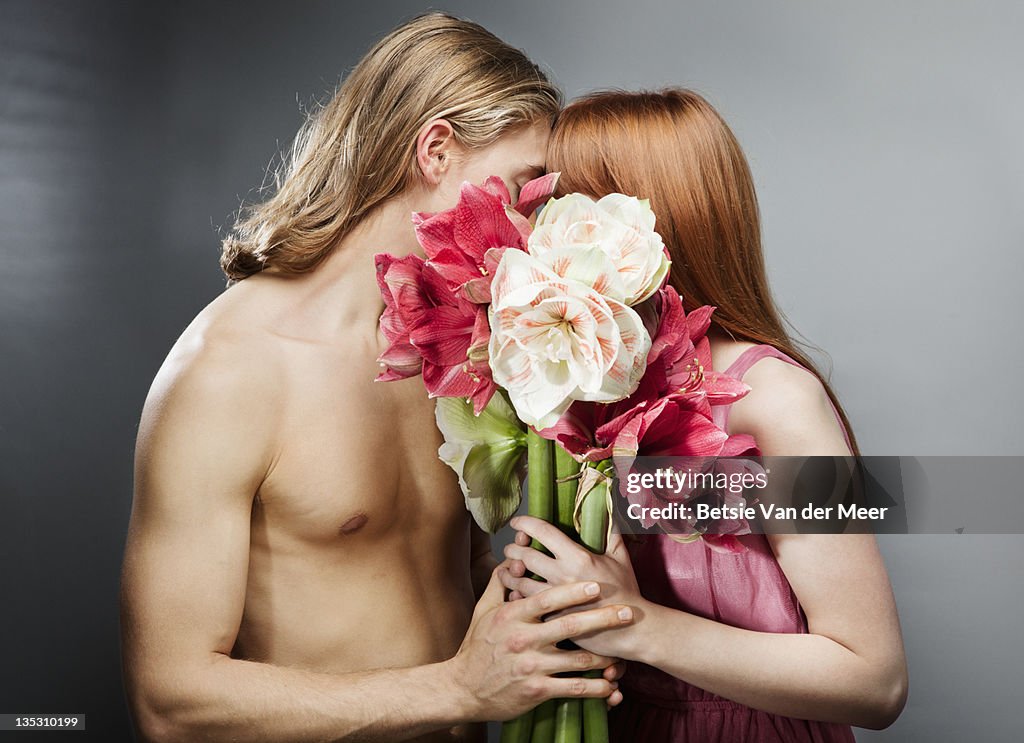 Couple kissing, hiding behind bouquet of flowers.