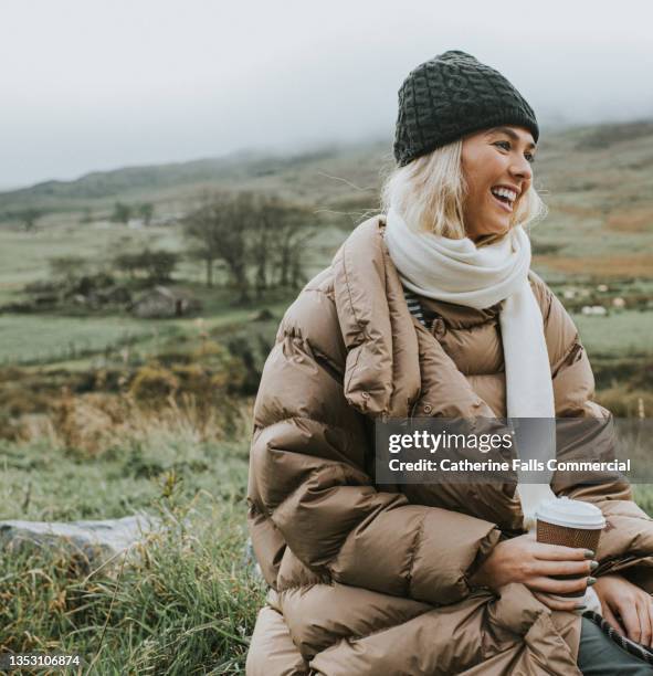 a beautiful young woman clutches a takeaway coffee cup, as she enjoys being outdoors - dunjacka bildbanksfoton och bilder