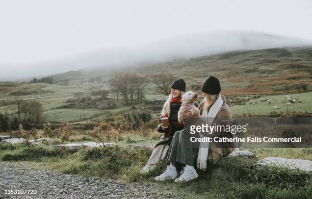 two young woman enjoy the great outdoors, while one holds an old west highland terrier on her knee - scottish culture photos et images de collection