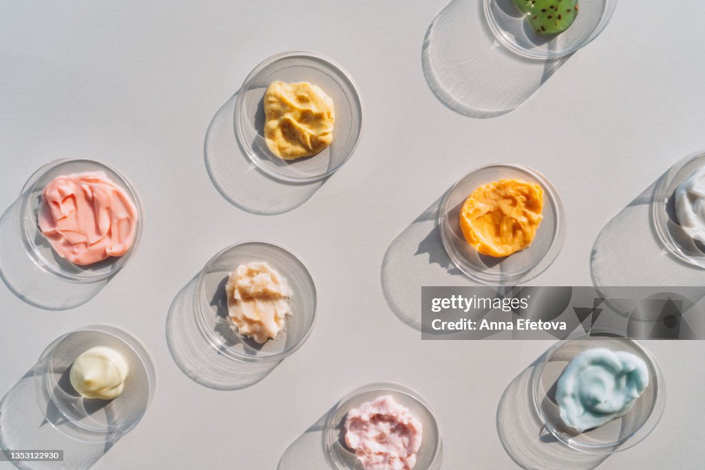 Multicolored creams and scrubs in many Petri dishes on gray background. Concept of cosmetics laboratory researches. Photography in flat lay style