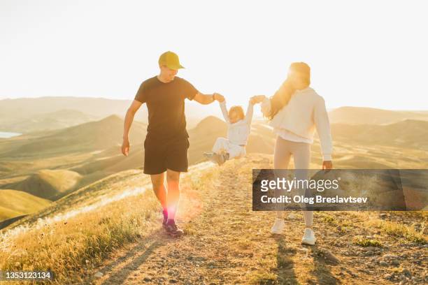 young and happy family walking with small daughter outdoors at sunset and laughing. - baby lachen natur stock-fotos und bilder