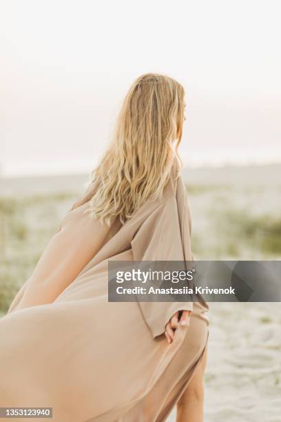 woman wearing beige silk developing dress against the seaside. - beach vibes stock-fotos und bilder
