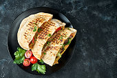 Three pita bread with vegetables, chicken and beef in a black plate on a dark background