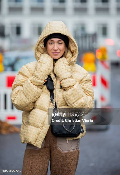Sonia Lyson is seen wearing sneaker New Balance, Prada bag, H&M pants in brown, Rotate down feather jacket with clipped gloves, Rotate beanie on...