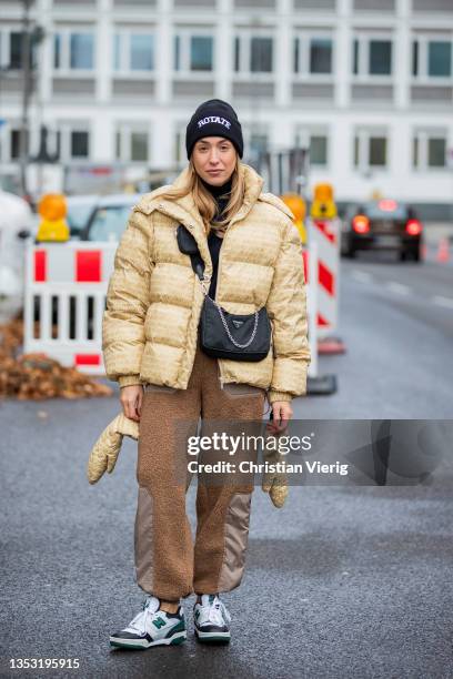 Sonia Lyson is seen wearing sneaker New Balance, Prada bag, H&M pants in brown, Rotate down feather jacket with clipped gloves, Rotate beanie on...