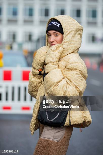 Sonia Lyson is seen wearing sneaker New Balance, Prada bag, H&M pants in brown, Rotate down feather jacket with clipped gloves, Rotate beanie on...