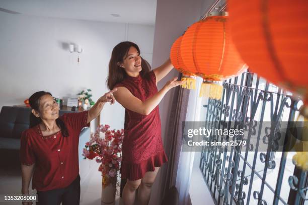 young granddaughter helping her grandmother preparing to hanging new red chinese lanterns - woman red lantern stock pictures, royalty-free photos & images