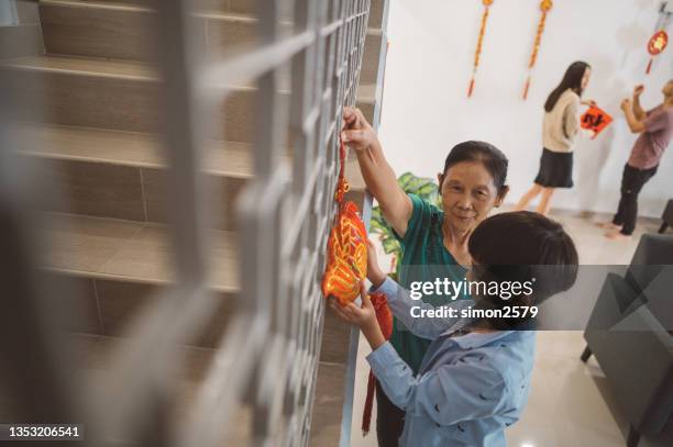 joyful grandmother decorating their house with her grandson preparing for chinese new year in living room - 39 year old stockfoto's en -beelden