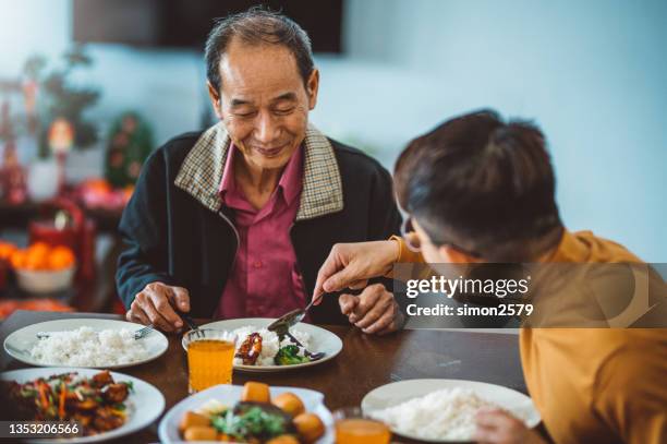 un homme asiatique partageant de la nourriture avec son père tout en profitant d’un dîner de retrouvailles à la maison pendant le nouvel an chinois - chinese new year food photos et images de collection