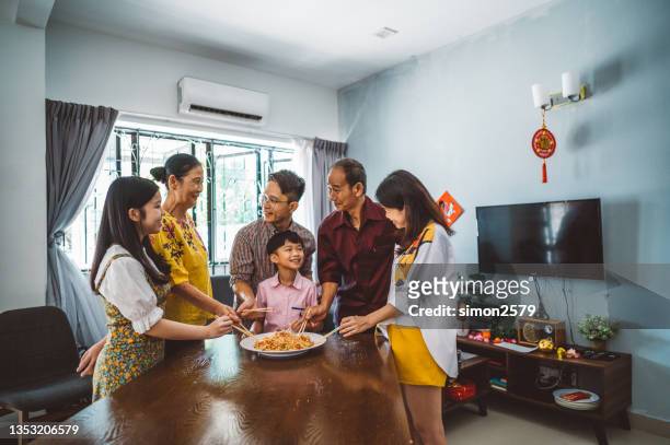 une famille asiatique célébrant le nouvel an chinois avec de la nourriture traditionnelle lou sang (plats de poisson cru) lors du dîner de réunion de famille - chinese new year food photos et images de collection