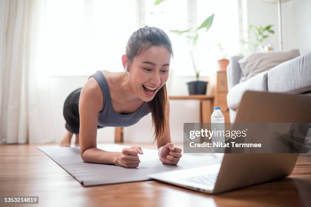 young woman fitness instructor using a laptop for doing an online class with the fitness community at her apartment. - asian female bodybuilder stock-fotos und bilder