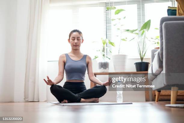 yoga improves strength, balance, and flexibility. young asian woman doing lotus pose to meditate at her apartment. office syndrome preventing, healthy lifestyle. - self discipline imagens e fotografias de stock