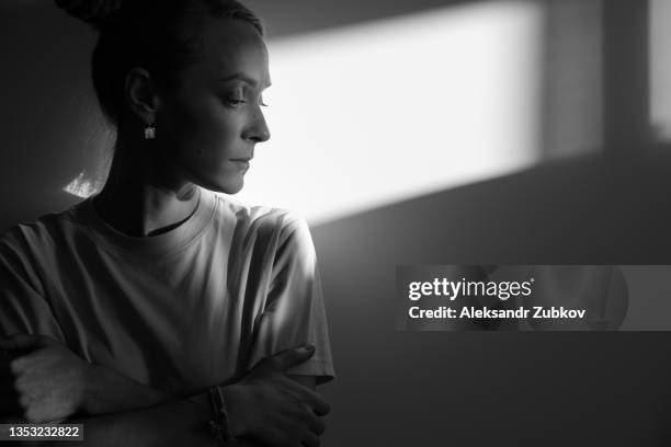 a lonely young sad calm girl or woman stands against a white wall, in a psychiatric clinic or at home, in the rays of sunlight, looking away. the concept of depression from illness and quarantine, fatigue and impotence. a copy of the space. - prisoner stock pictures, royalty-free photos & images