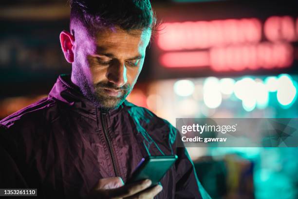 young man uses a smartphone at night in the city street. - efeito gel imagens e fotografias de stock