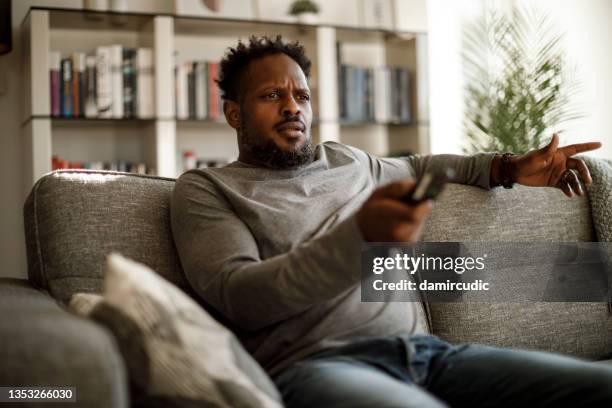 angry man watching tv at home - african american watching tv stock pictures, royalty-free photos & images