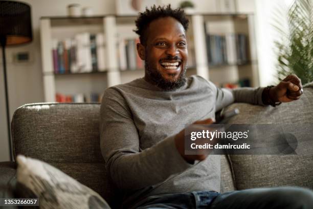 hombre emocionado animando mientras ve la televisión en casa - escandalo tv fotografías e imágenes de stock