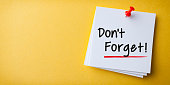 White Sticky Note With Don't Forget And Red Push Pin On Yellow Background