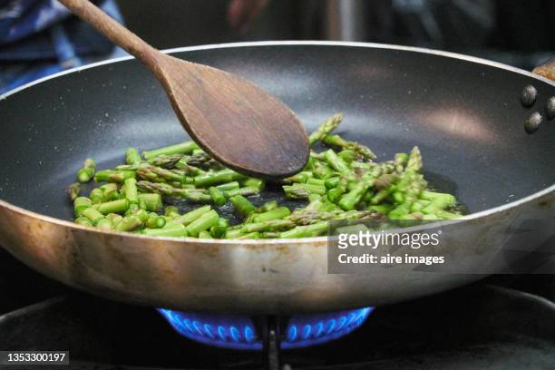 closeup of asparagus sauteed in a non-stick pan with a wooden ladle - angebraten stock-fotos und bilder