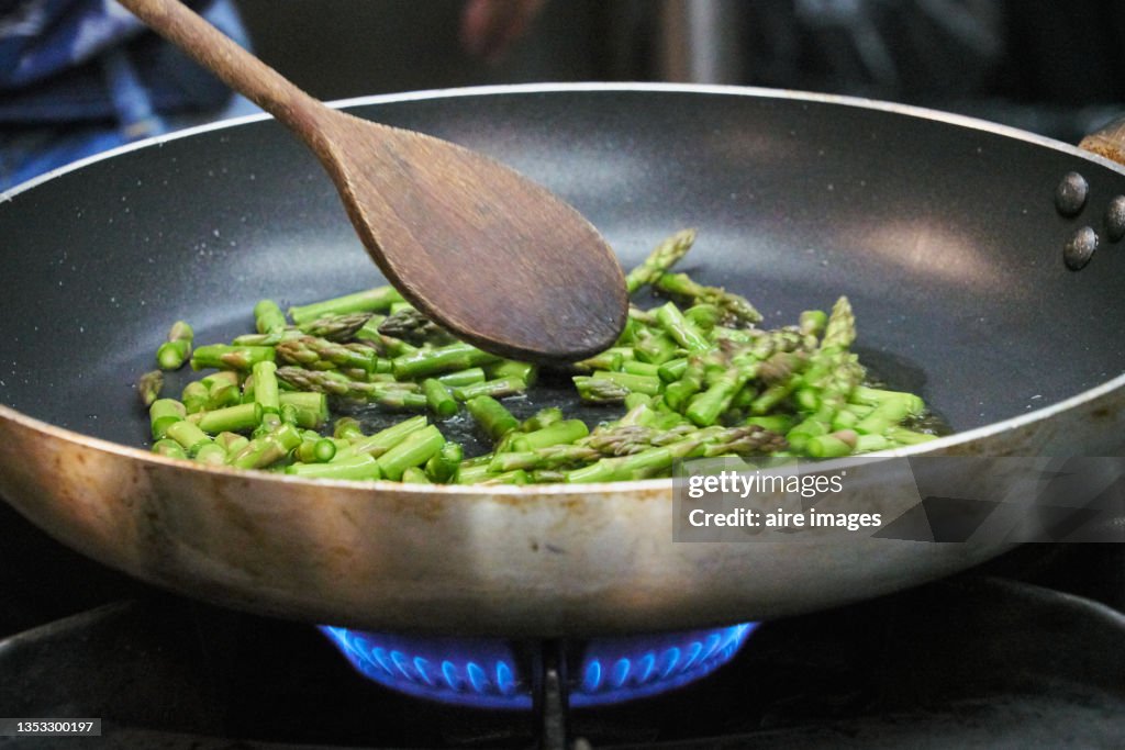 Closeup of asparagus sauteed in a non-stick pan with a wooden ladle