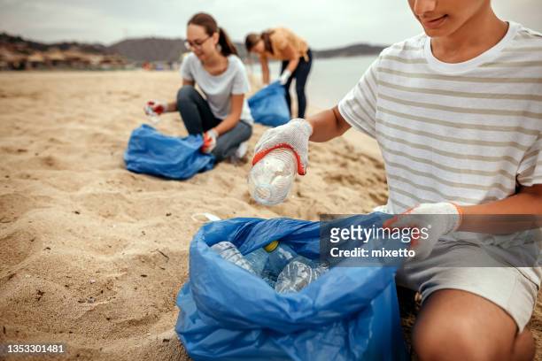 freiwillige reinigen den strand, indem sie müll in plastiktüten sammeln - umweltschutz reinigungsaktion stock-fotos und bilder