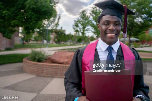 joven afroamericano mostrando con orgullo su diploma con una bata de graduación y una gorra después de graduarse de la universidad - haitian ethnicity fotografías e imágenes de stock
