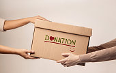 Donation Concept. The Volunteer Giving a Donate Box to the Recipient. Standing against the Wall