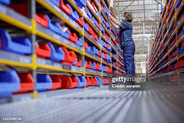 mulher com máscara facial organizando itens em bandejas em racks de armazém - industrial storage bins - fotografias e filmes do acervo