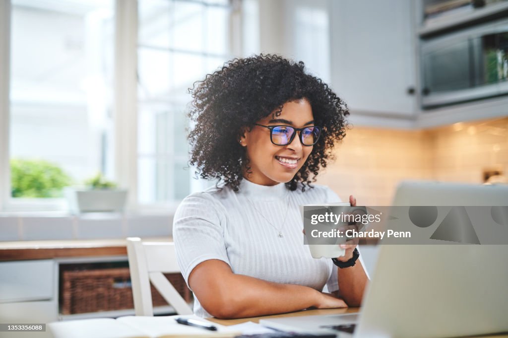 Shot of a young woman using a laptop and having coffee while working from