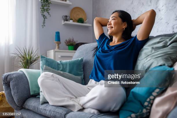 copy space shot of young woman lounging on sofa with hands behind head and daydreaming - huiselijk stockfoto's en -beelden