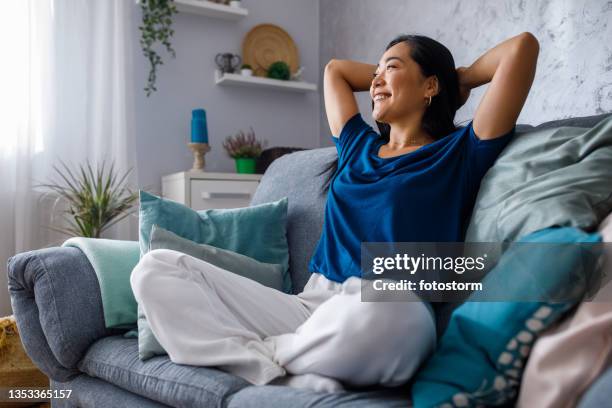 copy space shot of young woman lounging on sofa with hands behind head and daydreaming - hands behind head stock pictures, royalty-free photos & images