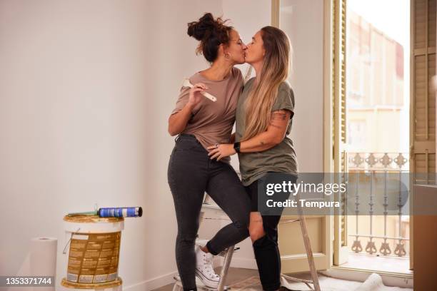 a female lgbt couple kisses each other while painting a new apartment. - images of lesbians kissing stock pictures, royalty-free photos & images
