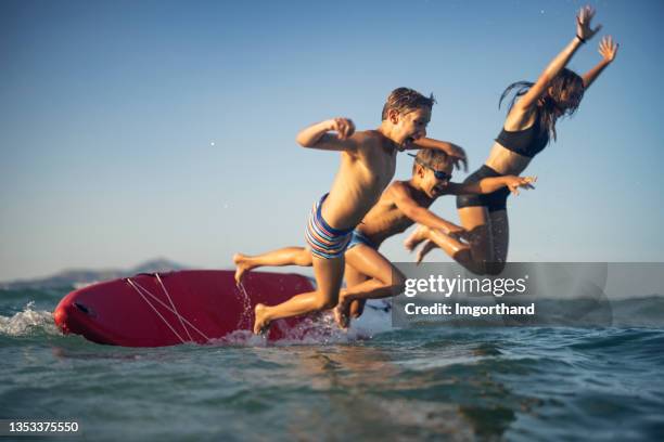 tre bambini che saltano dal paddleboard sup in mare - surf board foto e immagini stock