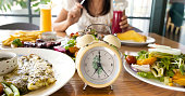 Selective focus of Alarm yellow clock  with Intermittent fasting IF diet concept and woman eating background