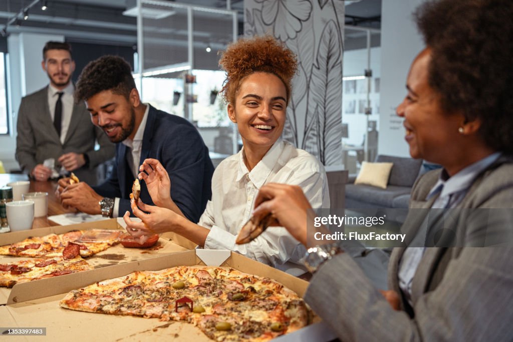 Funny and cheerful multiracial coworkers having a pizza for a lunch break