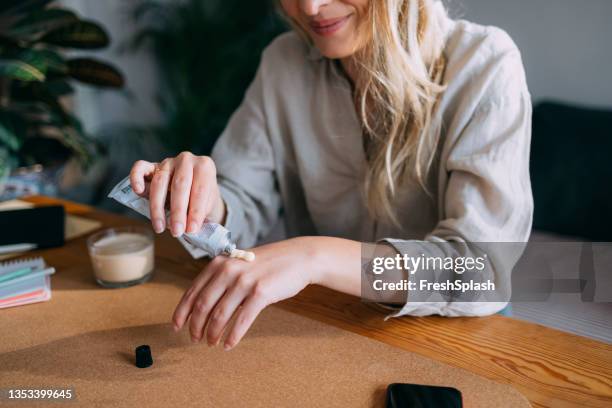 una donna anonima che applica una crema idratante sulle mani - crema mani foto e immagini stock