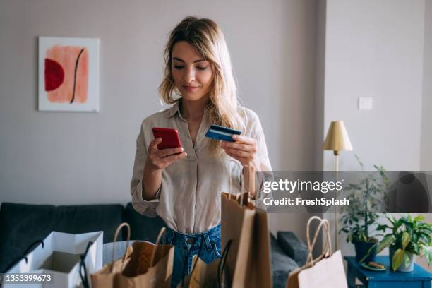 smiling woman using mobile phone and credit card for online shopping from home - online shopping stock pictures, royalty-free photos & images