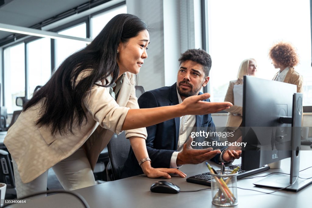 Disappointed Asian businesswoman, arguing with her mixed-race male coworker in the office