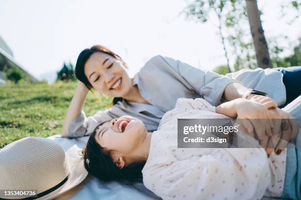 affectionate young asian mother and little daughter lying down on the grassy field, having fun playing and smiling joyfully, enjoying together on a sunny day. family love and bonding time. enjoying the nature. outdoor fun concept - child lying down stock pictures, royalty-free photos & images