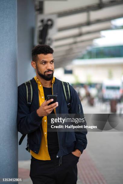 young man commuter at the bus station using smartphone and waiting for bus. - mann bus smartphone stock-fotos und bilder