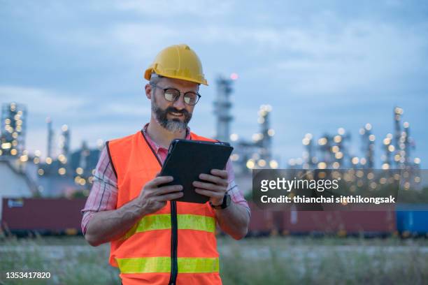 engineer wearing safety helmet using laptop at night with power plant background,power plant. - hard hat ipad stock pictures, royalty-free photos & images