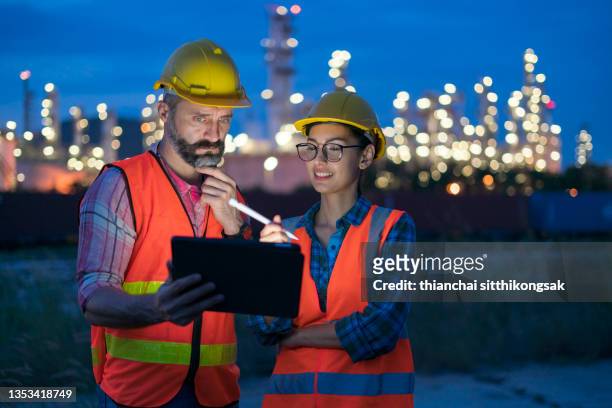 two engineer woman using digital tablet working late night with refinery plant on background. - premium gasoline stock pictures, royalty-free photos & images